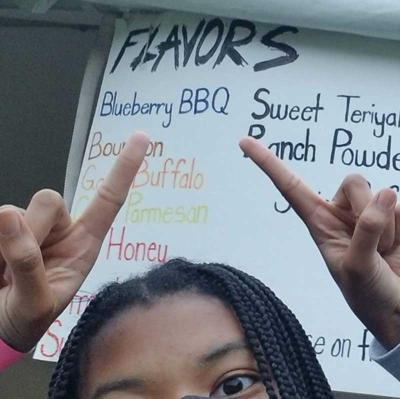 Eden Wilson, Lemonerdy, pointing at Blueberry Barbeque wings on the menu at the Michigan Chicken Wing Festival in Lansing, MI